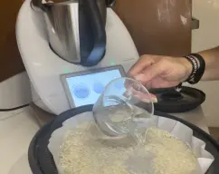 Step <p>En la bandeja del varoma colocamos papel vegetal... y extendemos sobre la superficie una taza de arroz y dos tazas de agua...</p><p><br></p> illustration