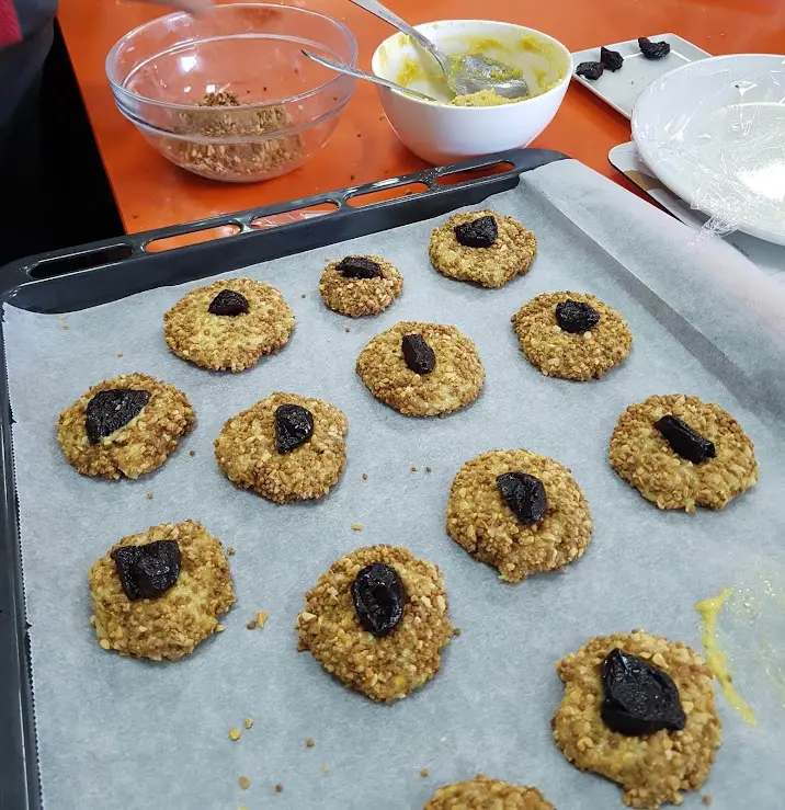 Step Añada la almendra molida, la levadura, el huevo y el agua de azahar. Mezcle 12 seg/vel 4. Forme 16 bolas del tamaño de una nuez, aplástelas y reboce con el granillo de almendra. Colóquelas en la bandeja preparada y ponga ½ ciruela pasa en el centro. illustration